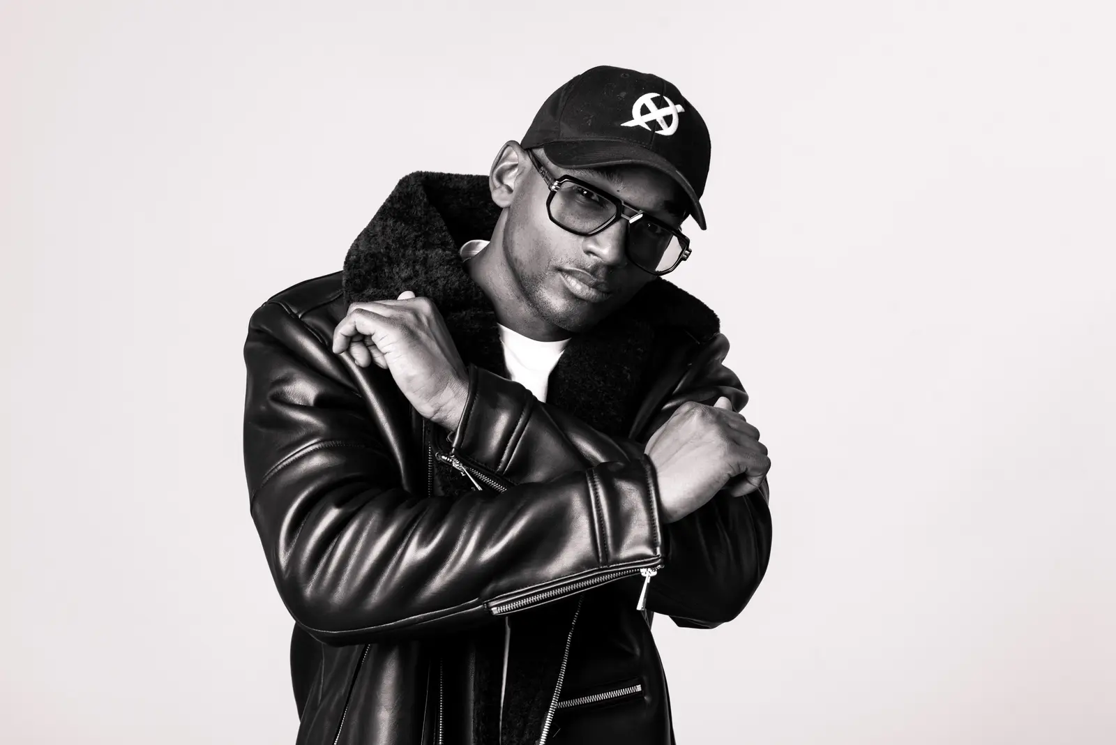 Hurrican&nbsp;X in a black cap and leather jacket, arms crossed, studio portrait